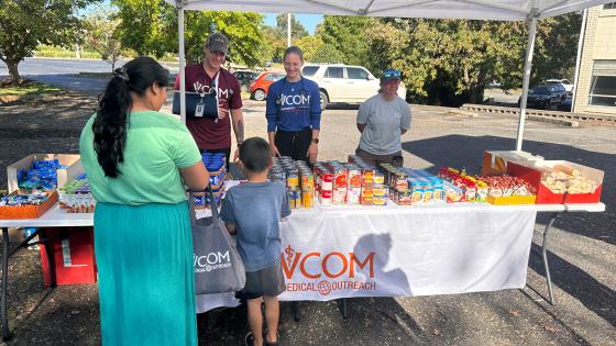 VCOM Outreach table with free food. Mother and child picking up food